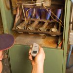 Gas furnace repairman holding instrument in front of furnace